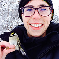 A college professor wearing glasses holds a tiny bird